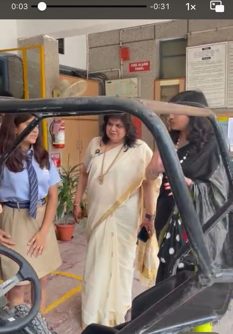 Visitors including a guest in a white sari gathered around the electric vehicle at the Shri Ram tech fest exhibition stand.